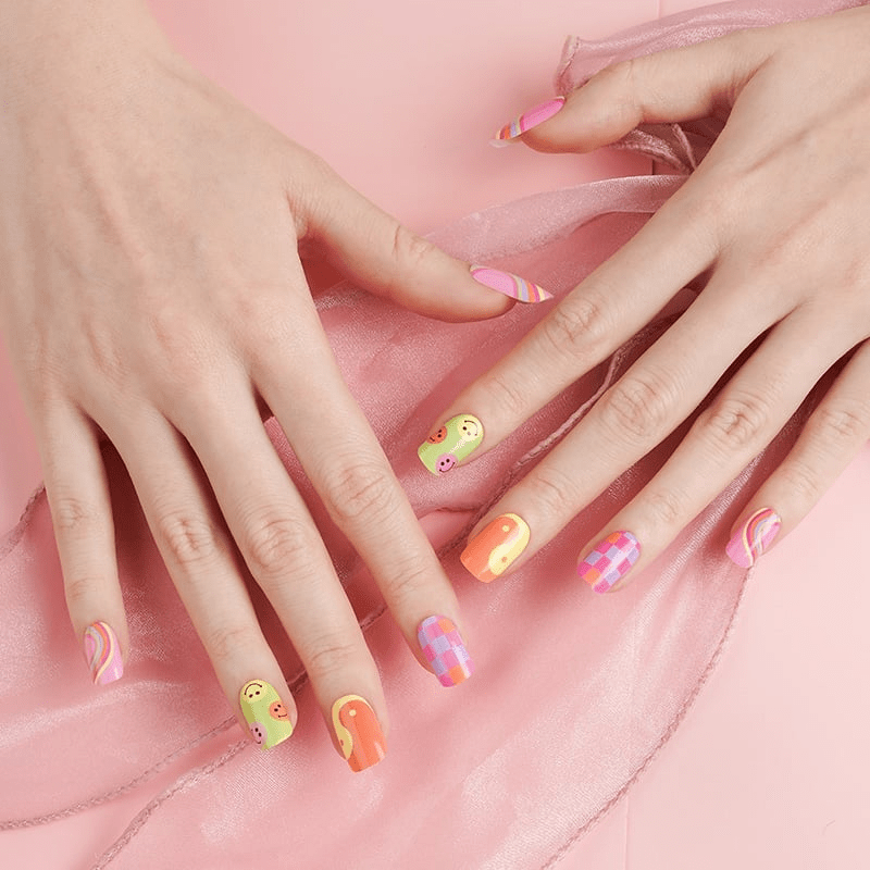 Two hands displaying retro nail art with smiley faces and geometric patterns in vibrant colours