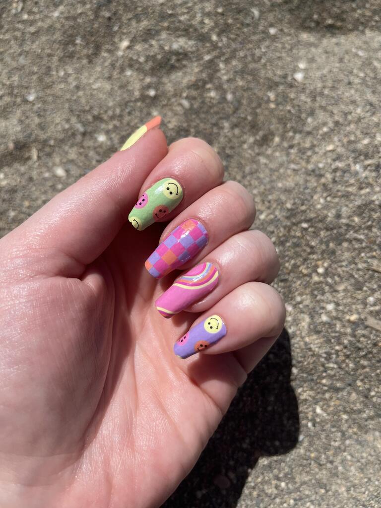 Hand displaying festival nail art featuring smiley face and checkered pattern nail wraps in bright hues