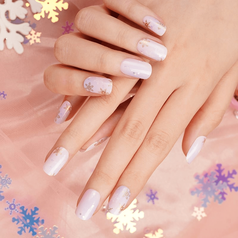 Hands wearing pink gradient nail wraps with delicate gold snowflakes for festive nail art