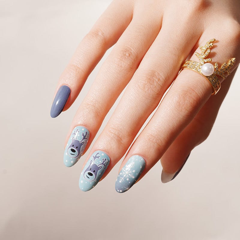 Hand wearing festive nail wraps in blue shades with white snowflake and reindeer nail art