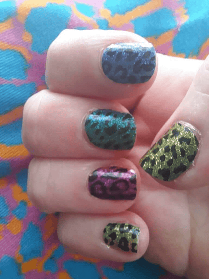 Glittery leopard print nail wraps on hand with vibrant multicoloured animal print patterns