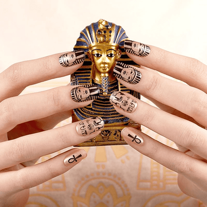 Hands displaying Egyptian themed nail wraps with gold pharaoh faces and hieroglyphic ankh symbols