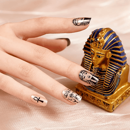 Hand with Egyptian pharaoh nail wraps beside golden sphinx ornament showing themed nail art