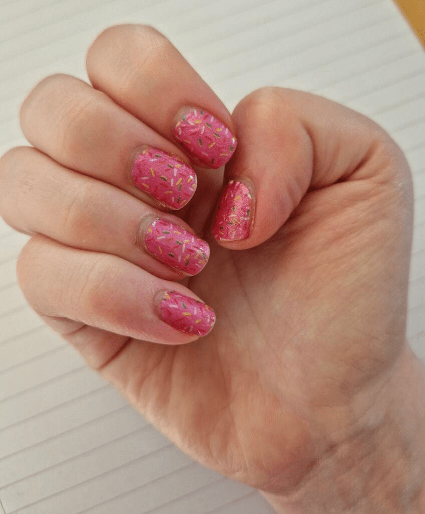 Pink sprinkles nail art design on hand showing playful confetti pattern manicure