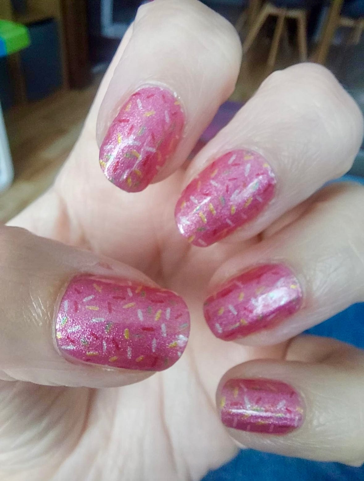 Pink glittery nail wraps with holographic sprinkles pattern on hand for at-home manicure