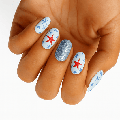 Hand showcasing white nail wraps with red and blue starfish patterns plus glitter accent nail