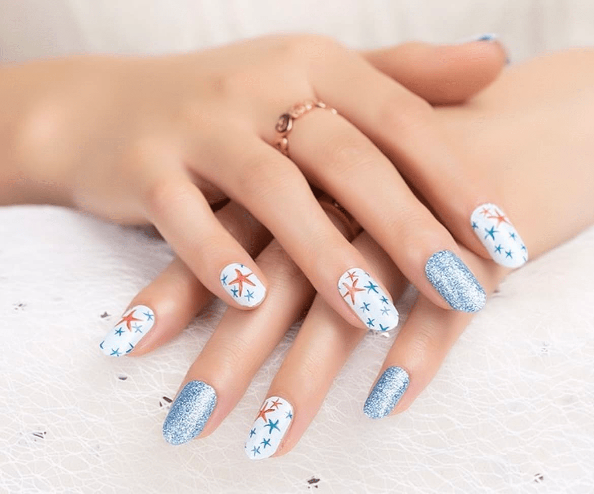 Manicured hands displaying starfish patterned nail wraps with blue glitter accent nails