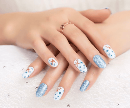 Manicured hands displaying starfish patterned nail wraps with blue glitter accent nails