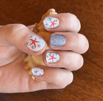 Clenched fist showing nautical starfish nail art wraps with sparkly blue glitter nail