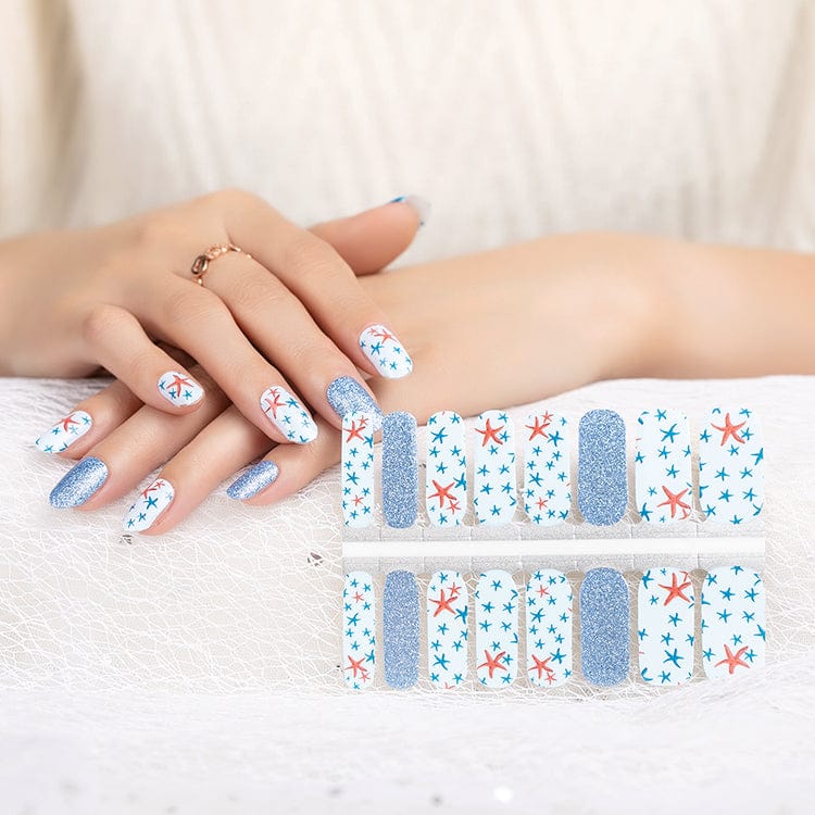 Hands with nail wrap sheet displaying starfish pattern designs and blue glitter strips