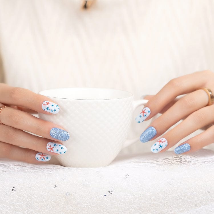 Hands holding white mug wearing nautical starfish nail wraps with blue glitter accents