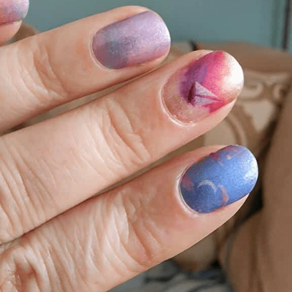 Close-up starry night nail wraps on fingertips blue purple gradient cosmic manicure design