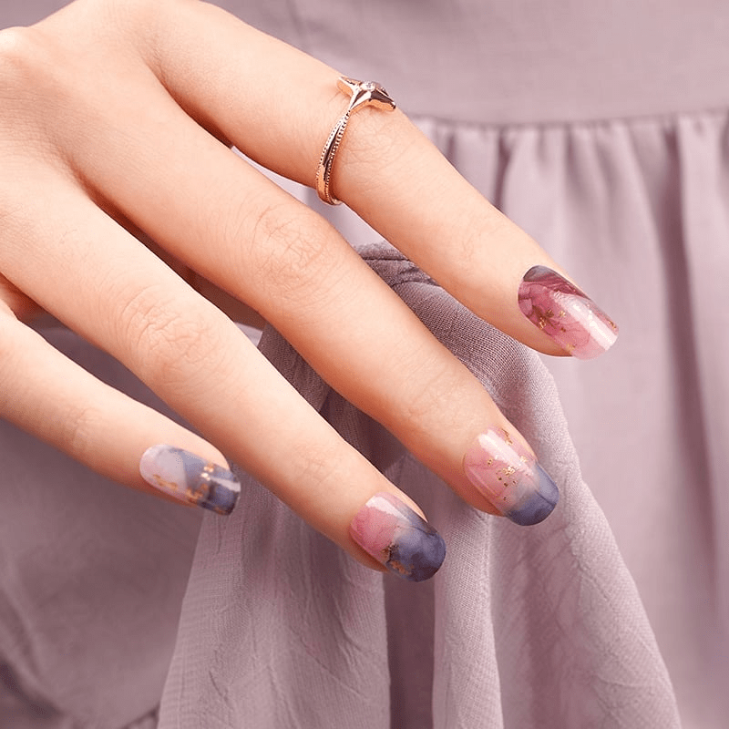 Hand with ring displaying abstract marble nail wraps in pink navy watercolour finish