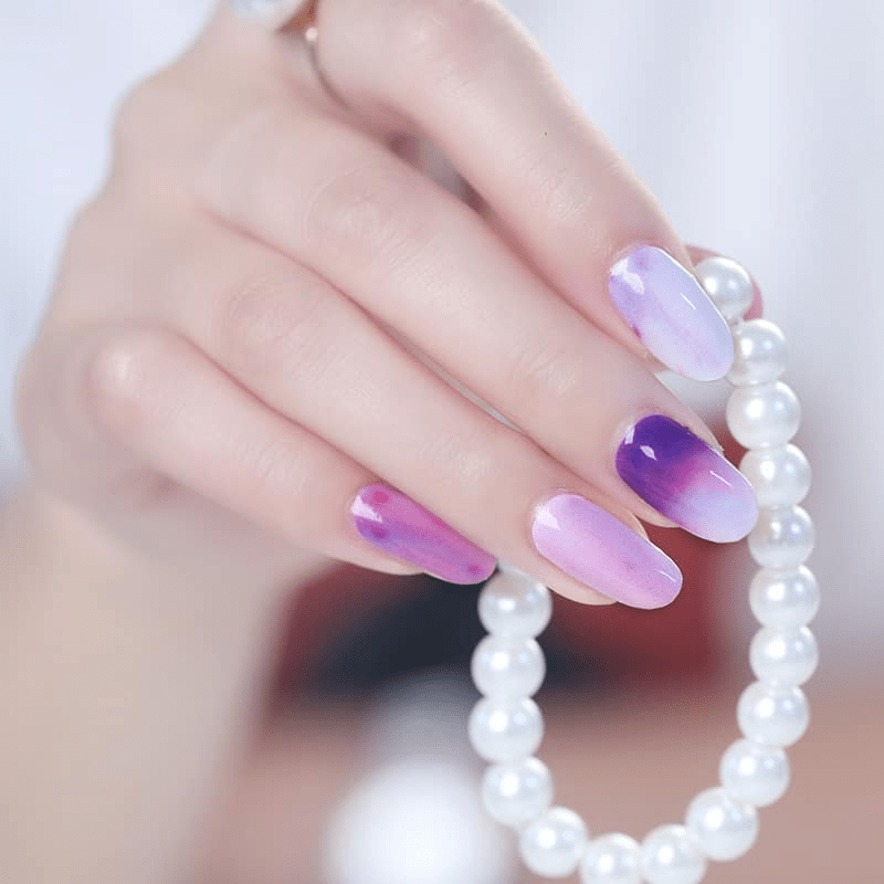 Lavender to purple ombre gel nail wraps on hand with pearl bracelet