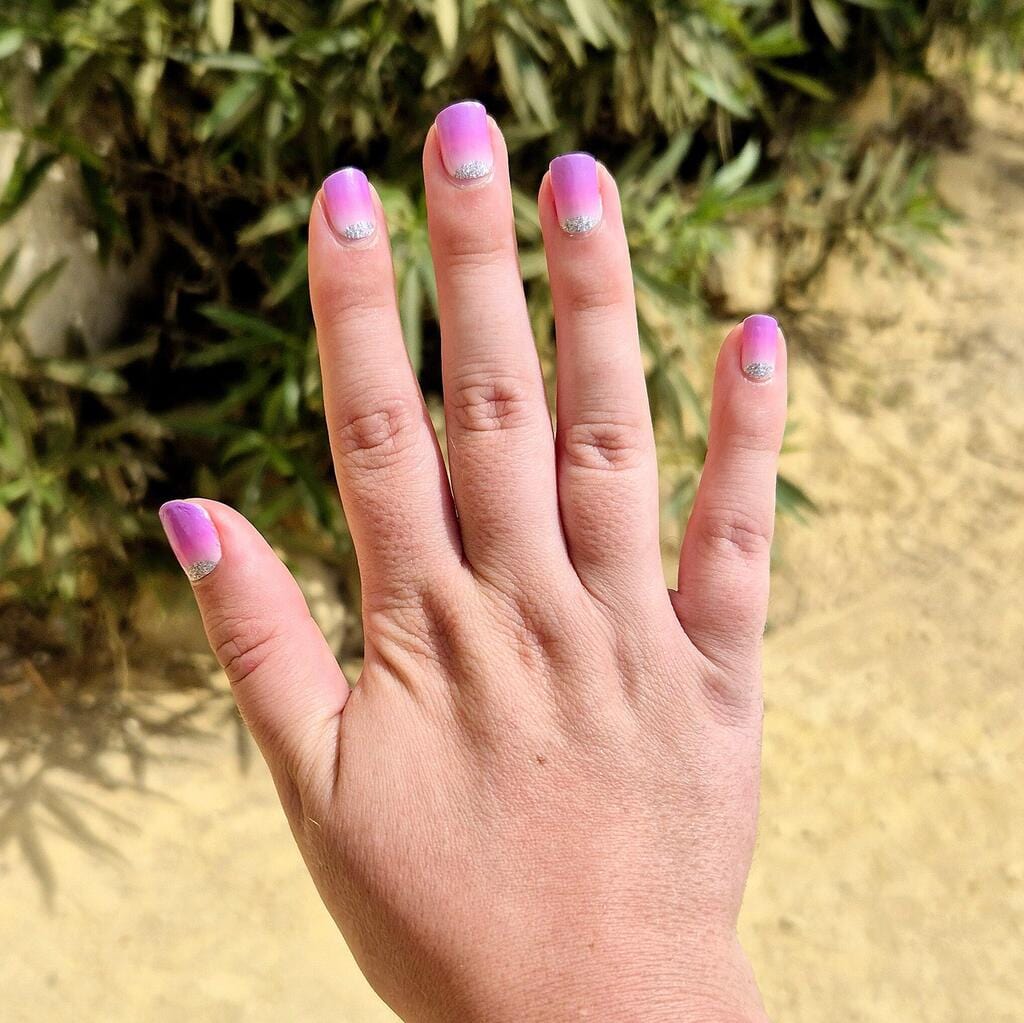 Hand wearing purple to pink ombre nail wraps with silver glitter French tips