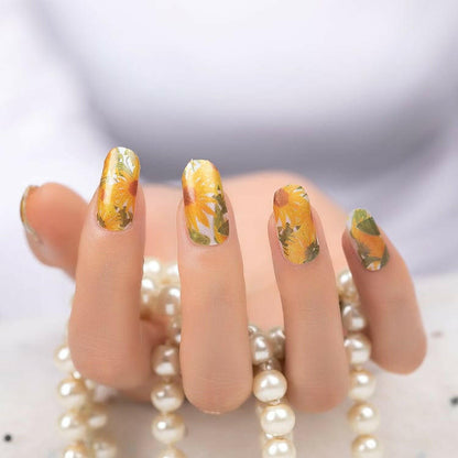 Hand wearing yellow sunflower watercolour nail wraps with pearl bracelet