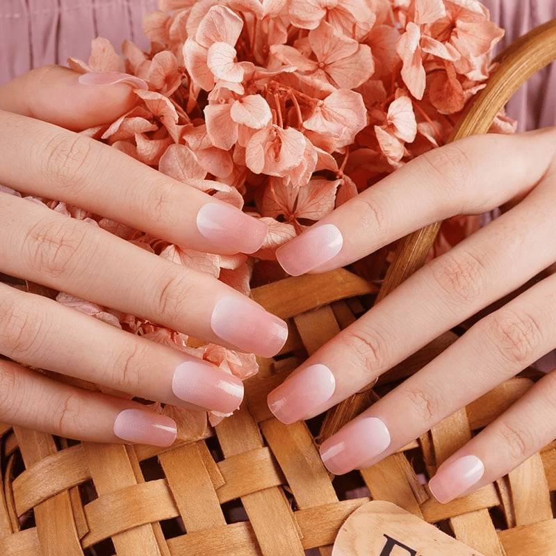 Hands with coral pink nail wraps holding wicker basket of peach flowers