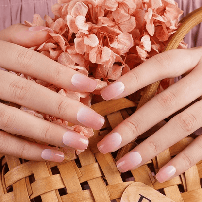 Hands with coral pink nail wraps holding wicker basket of peach flowers