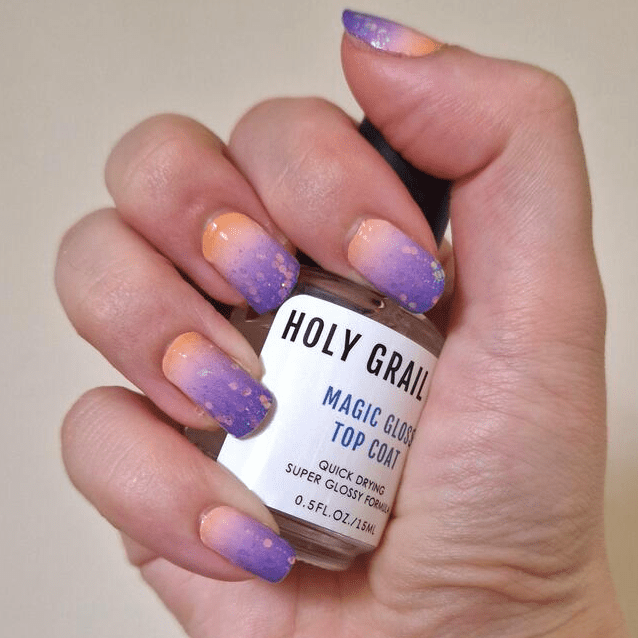 Hand holding magic gum top coat with purple to peach gradient glitter nail art