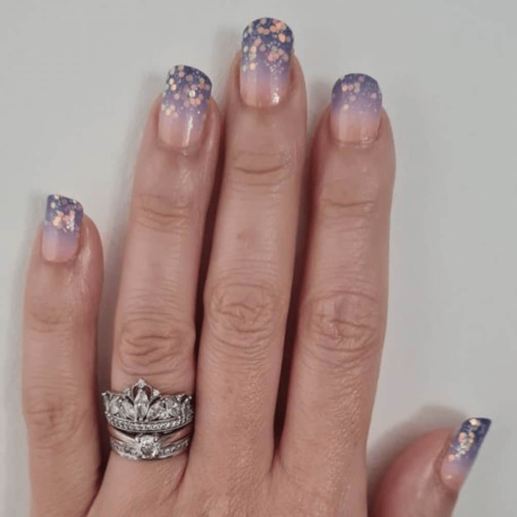 Hand wearing purple glitter ombre nail wraps with gradient sunset design and sparkles