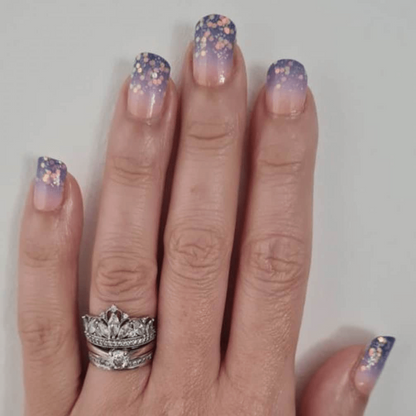Hand wearing purple glitter ombre nail wraps with gradient sunset design and sparkles