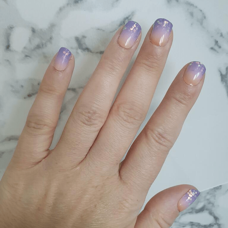 Purple gradient nail wraps on hand showing ombre glitter manicure with sparkle finish