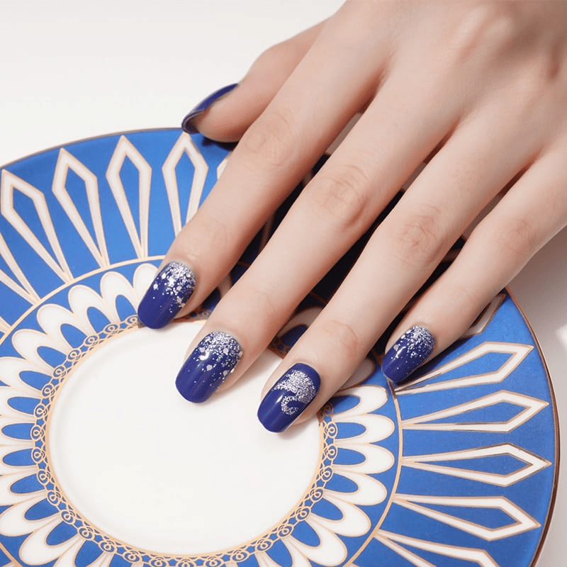 Blue nail wraps with silver swan design on decorative plate showcasing at-home manicure