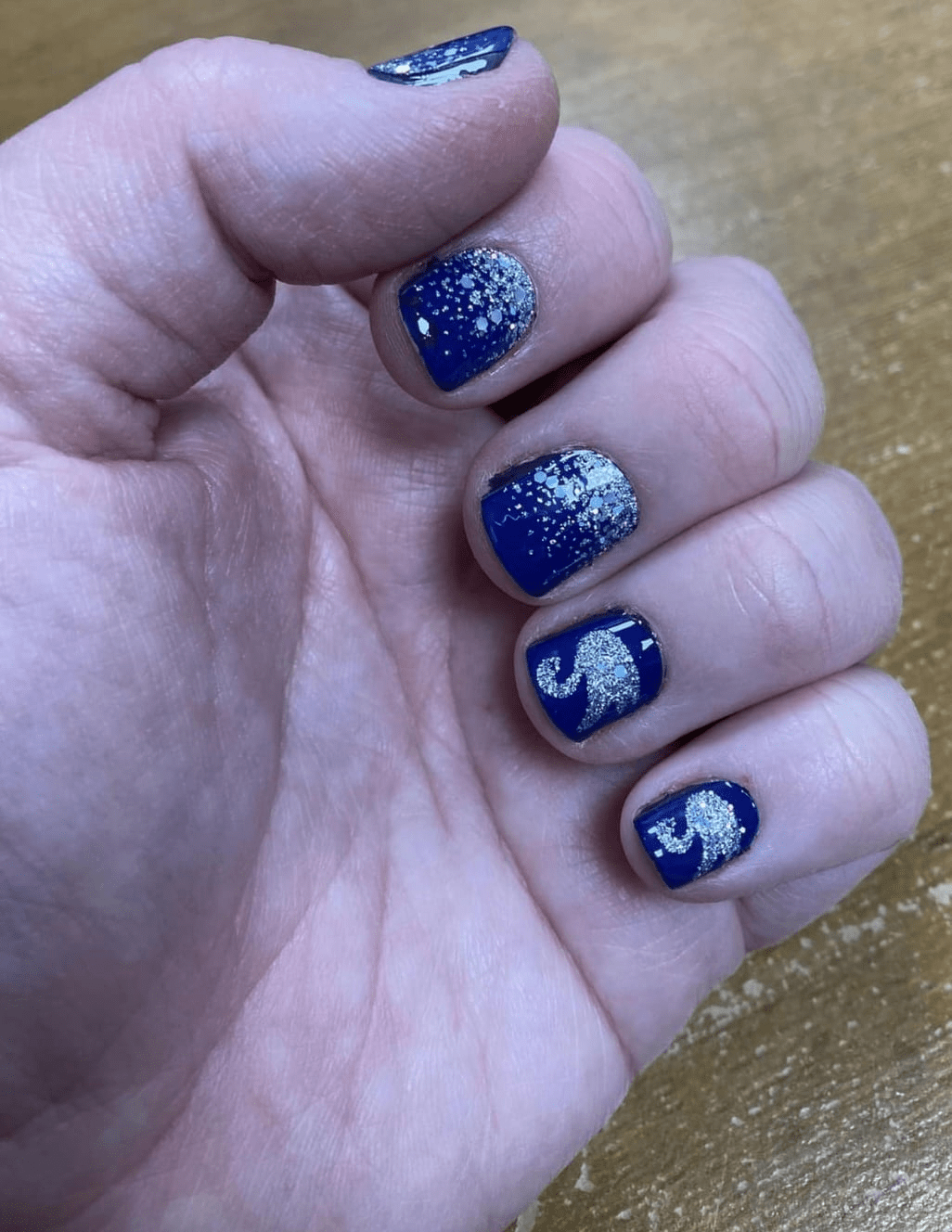 Close-up of blue nail wraps featuring silver swan and glitter design on fingers