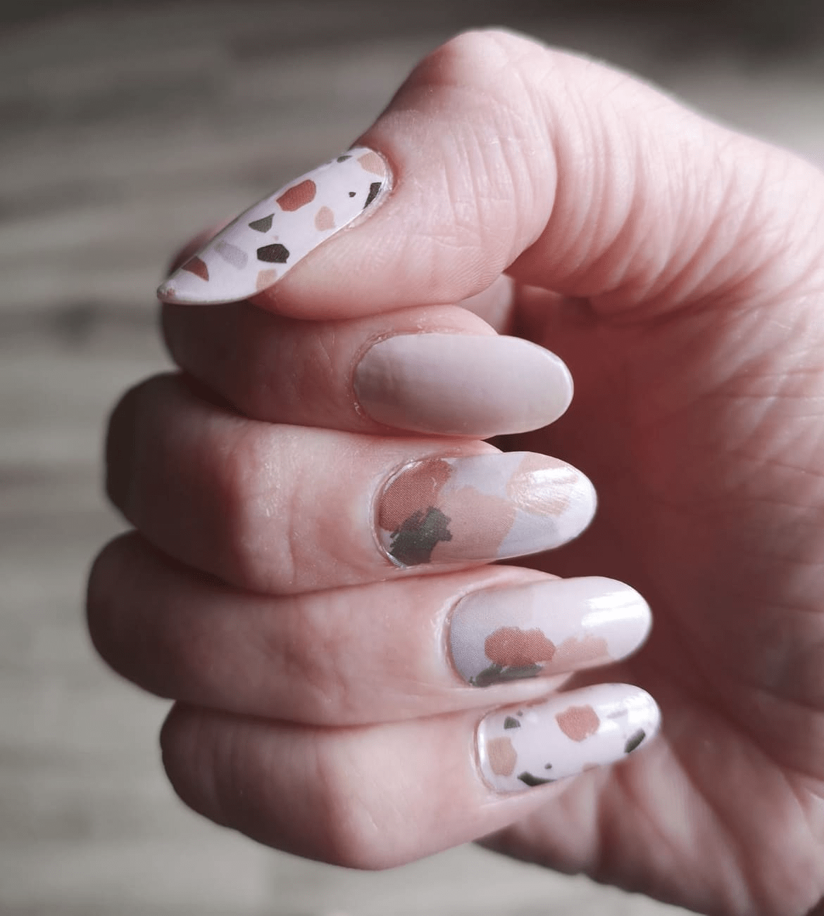 Terrazzo speckled nail wraps on hand showing nude base with grey stone pattern