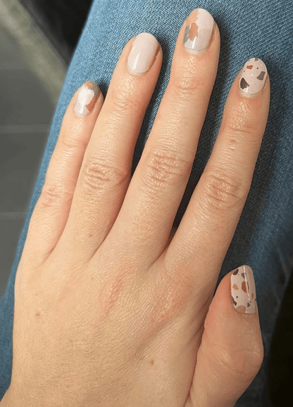 Hand displaying terrazzo nail art wraps with neutral speckled stone design