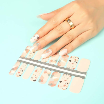 Hand with terrazzo nail wraps next to sheet showing speckled stone pattern