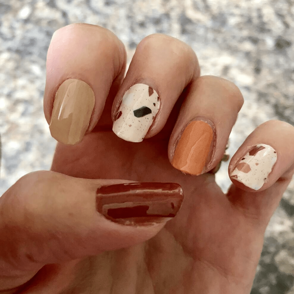 Autumn terrazzo nail art on hand with brown orange and cream speckled pattern