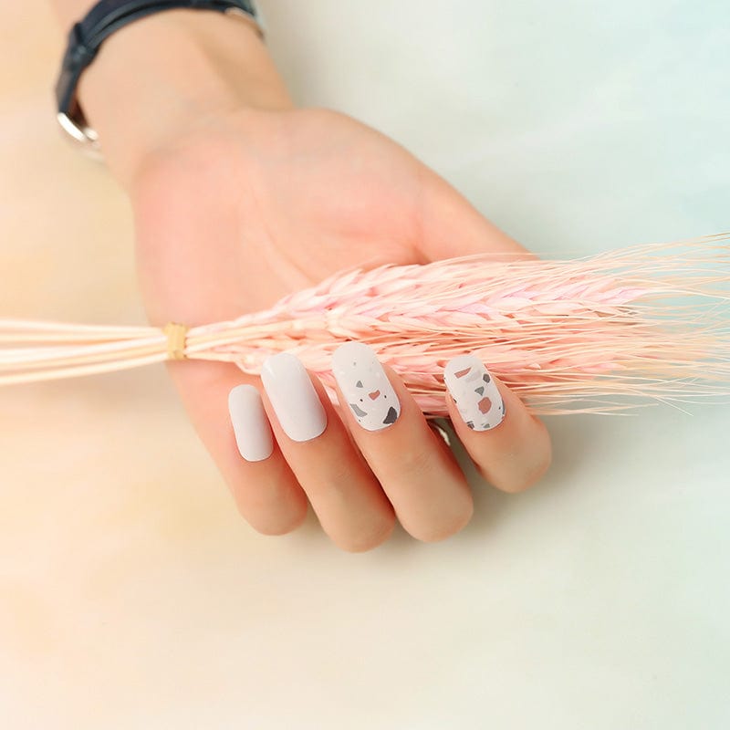 Hand wearing terrazzo nail art wraps with neutral speckled stone design for professional manicures