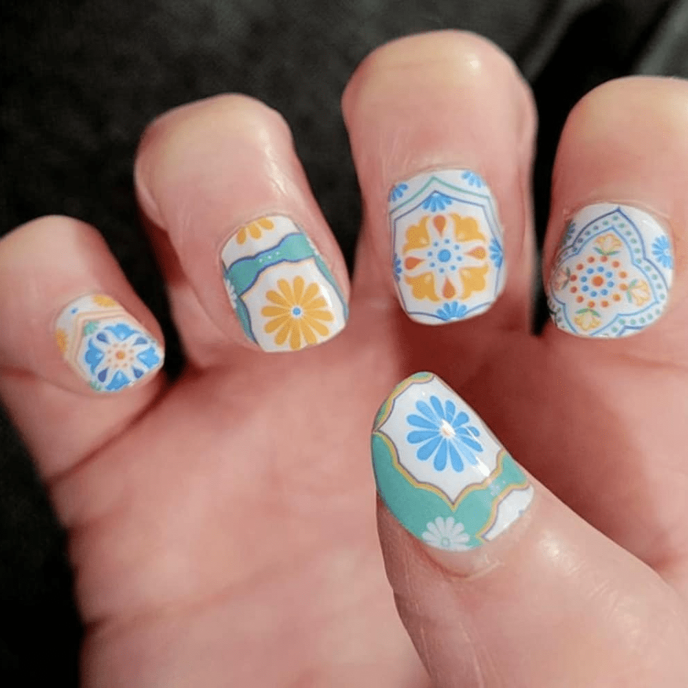 Blue orange floral nail wraps on hand showing retro 70s daisy patterns