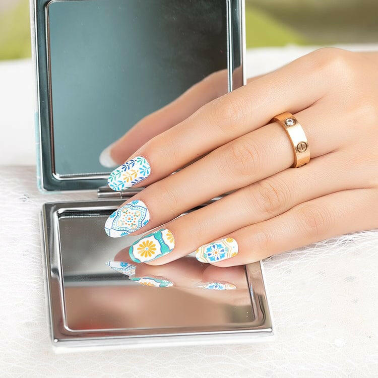 Hand holding mirror displaying vintage floral nail wraps with blue orange geometric designs