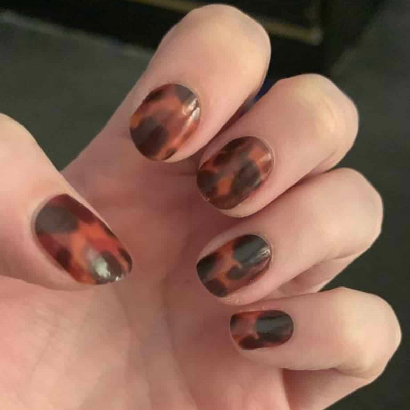 Tortoiseshell nail wraps on hand showing brown amber animal print pattern