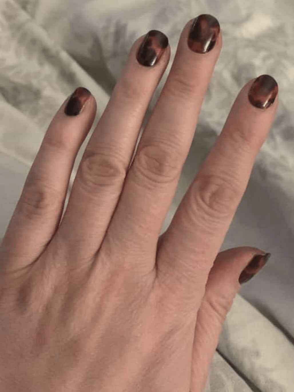 Tortoiseshell nail wraps on hand displaying brown and amber marbled animal print design