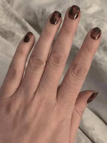 Tortoiseshell nail wraps on hand displaying brown and amber marbled animal print design