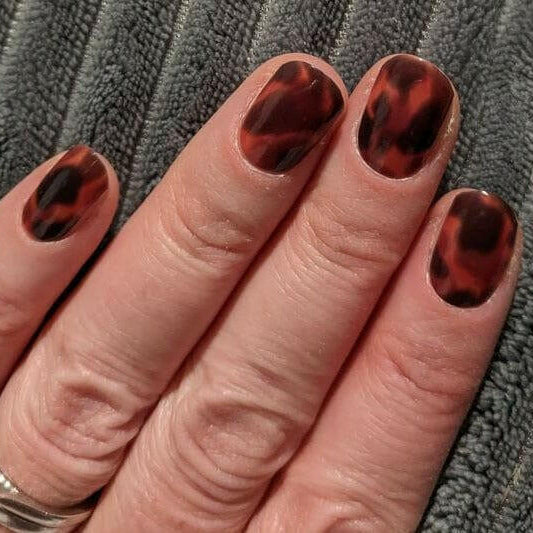 Brown tortoiseshell animal print nail wraps displayed on hand against grey fabric