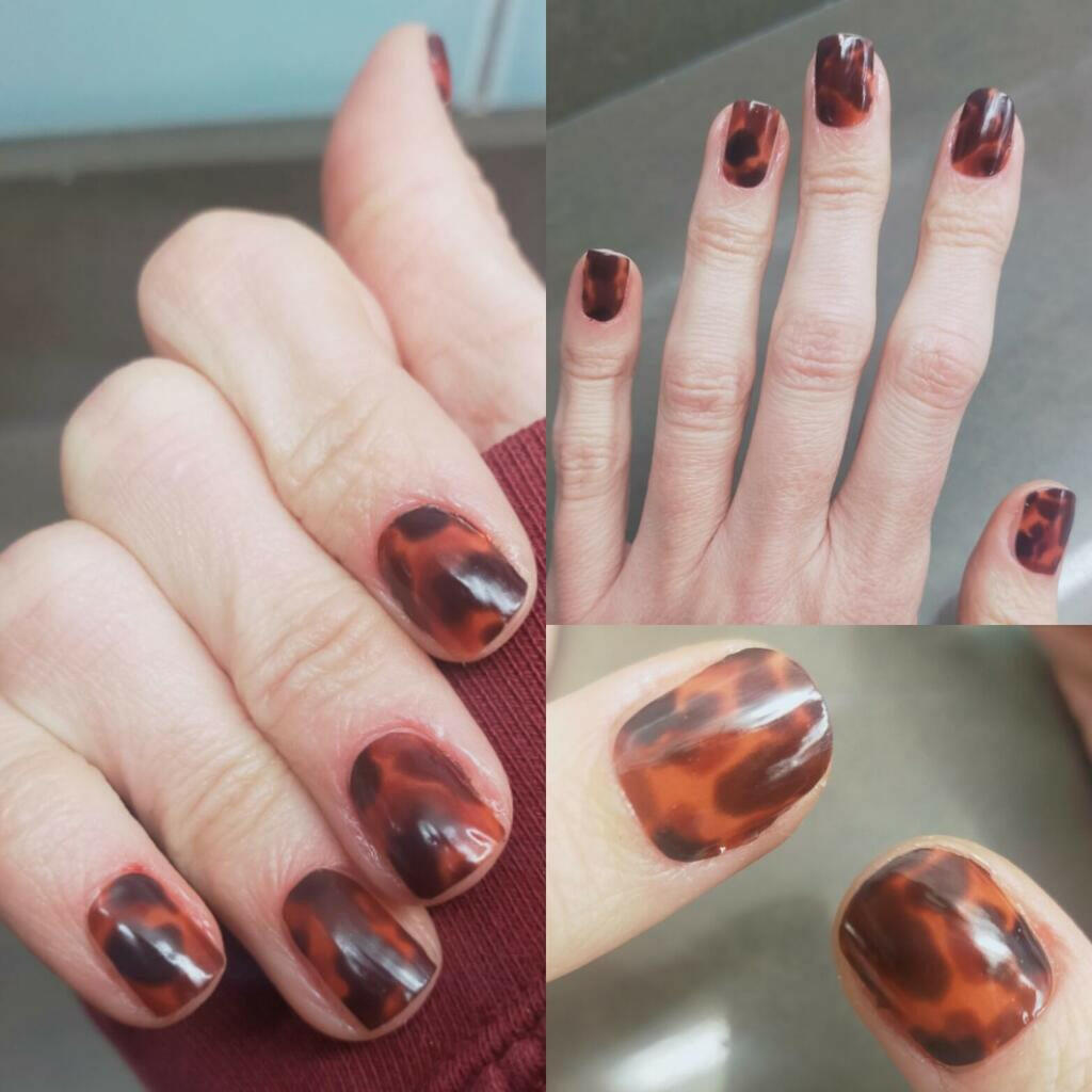 Brown tortoiseshell nail wraps on hands showing glossy amber animal print pattern
