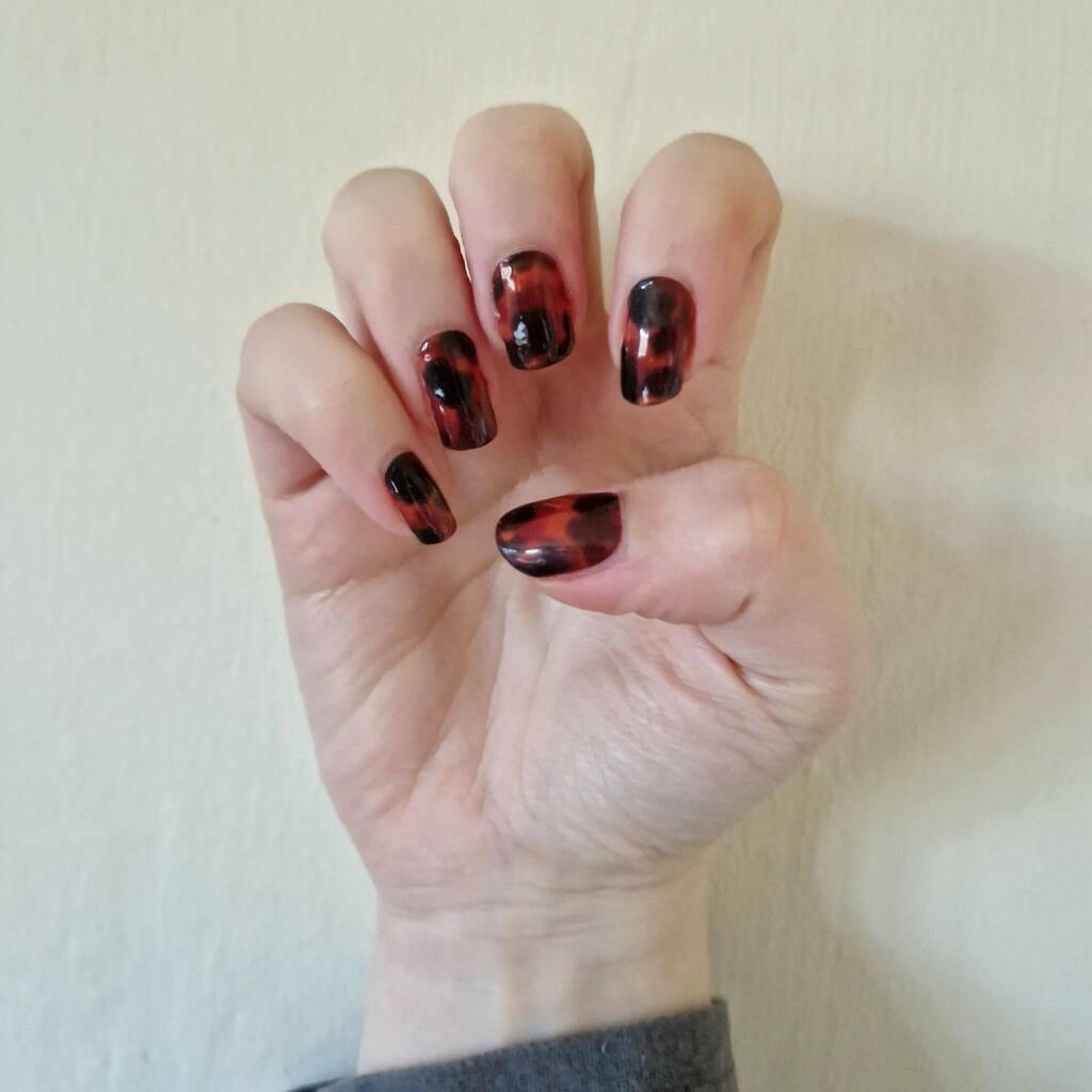 Hand showcasing glossy tortoiseshell nail wraps with brown amber animal print pattern