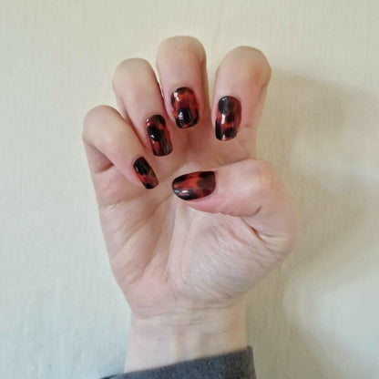 Hand showcasing glossy tortoiseshell nail wraps with brown amber animal print pattern