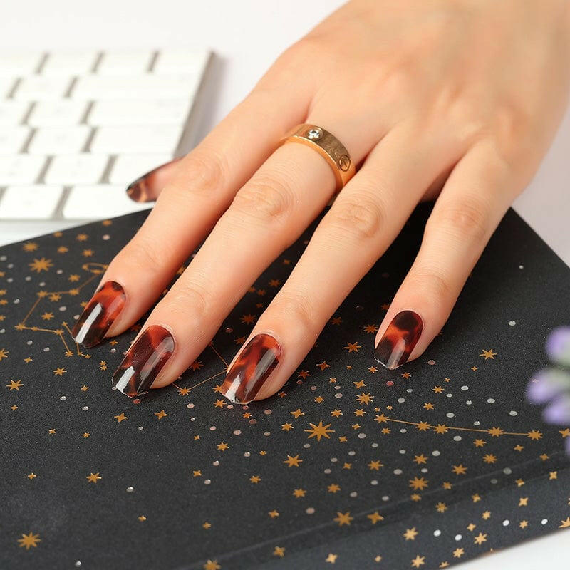 Hand with tortoiseshell nail wraps on starry notebook showcasing brown animal print design