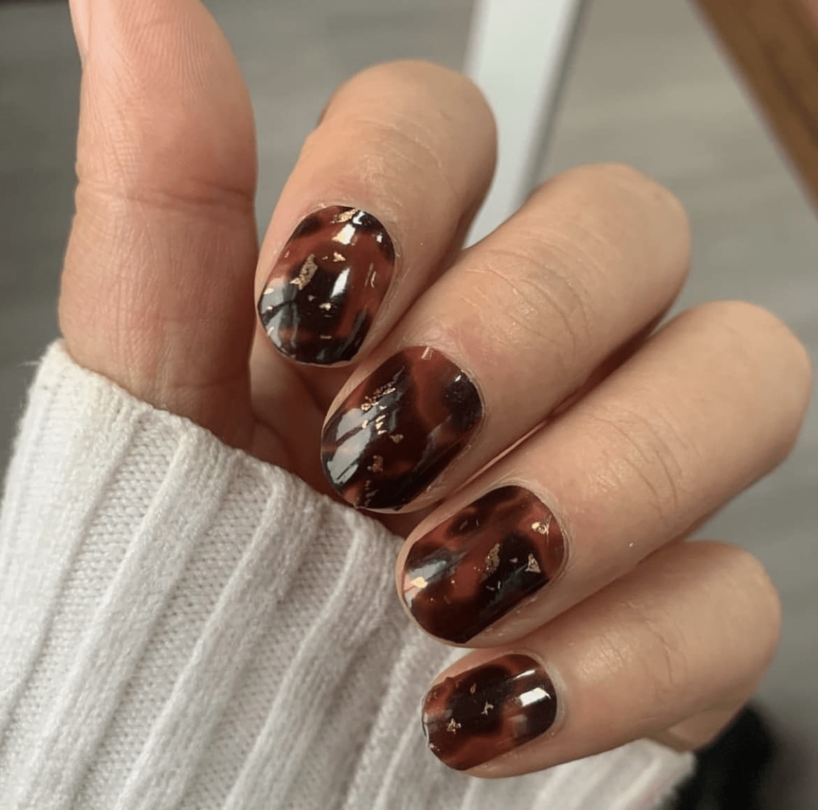 Glossy tortoiseshell pattern nail wraps with metallic gold details on fingers