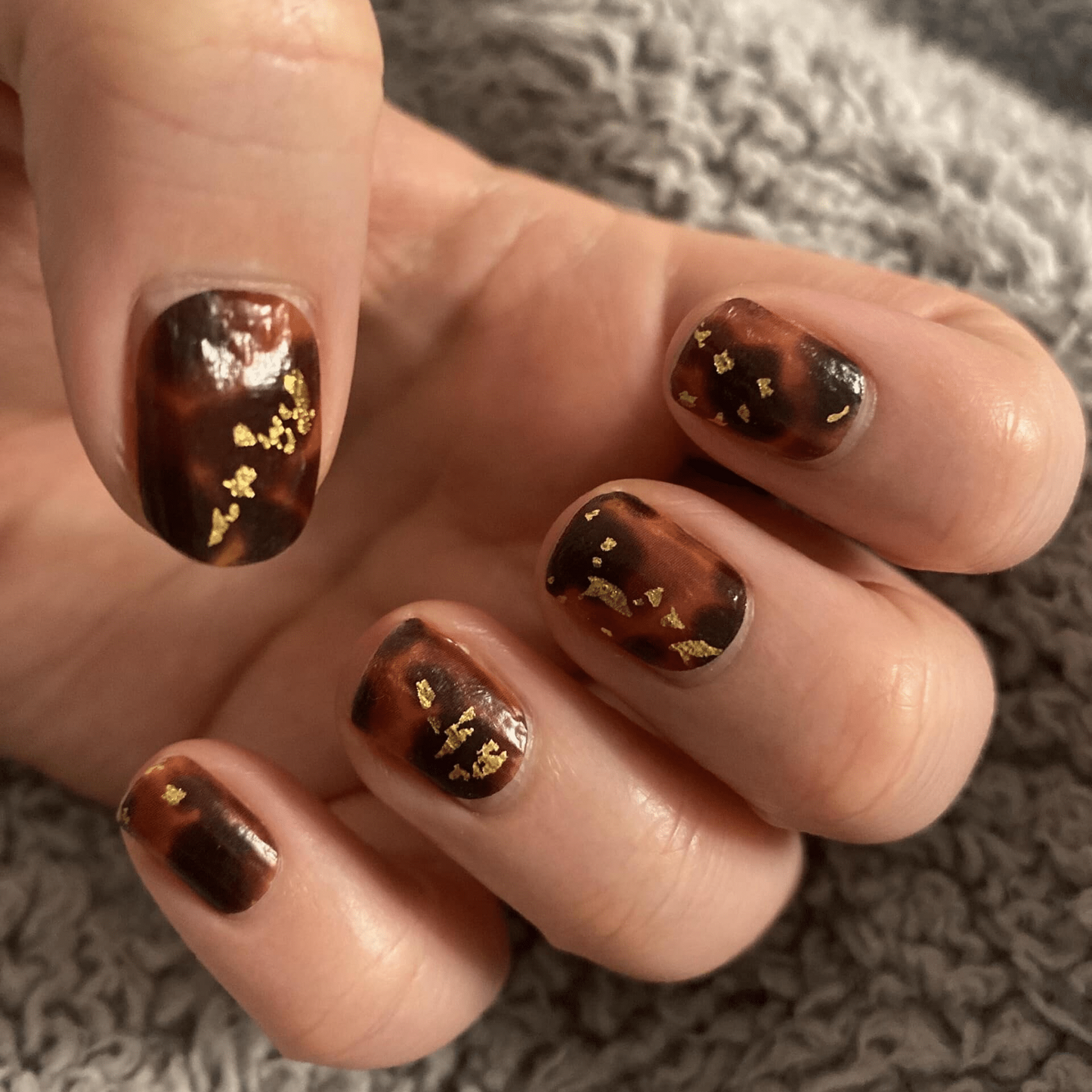 Brown tortoiseshell non-UV nail wraps with gold foil accents on hand