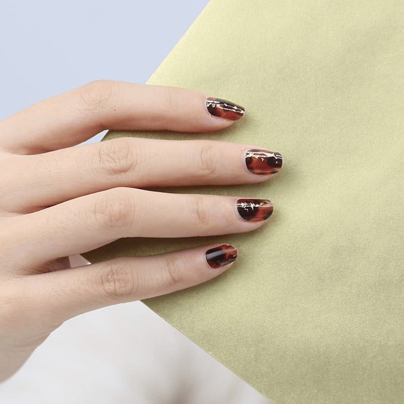 Hand showing brown tortoiseshell nail art wraps with gold foil highlights
