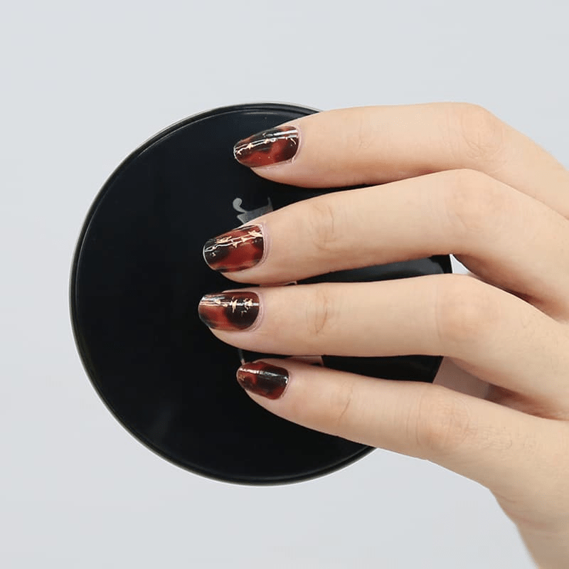 Tortoiseshell nail wraps with gold metallic accents displayed on black surface