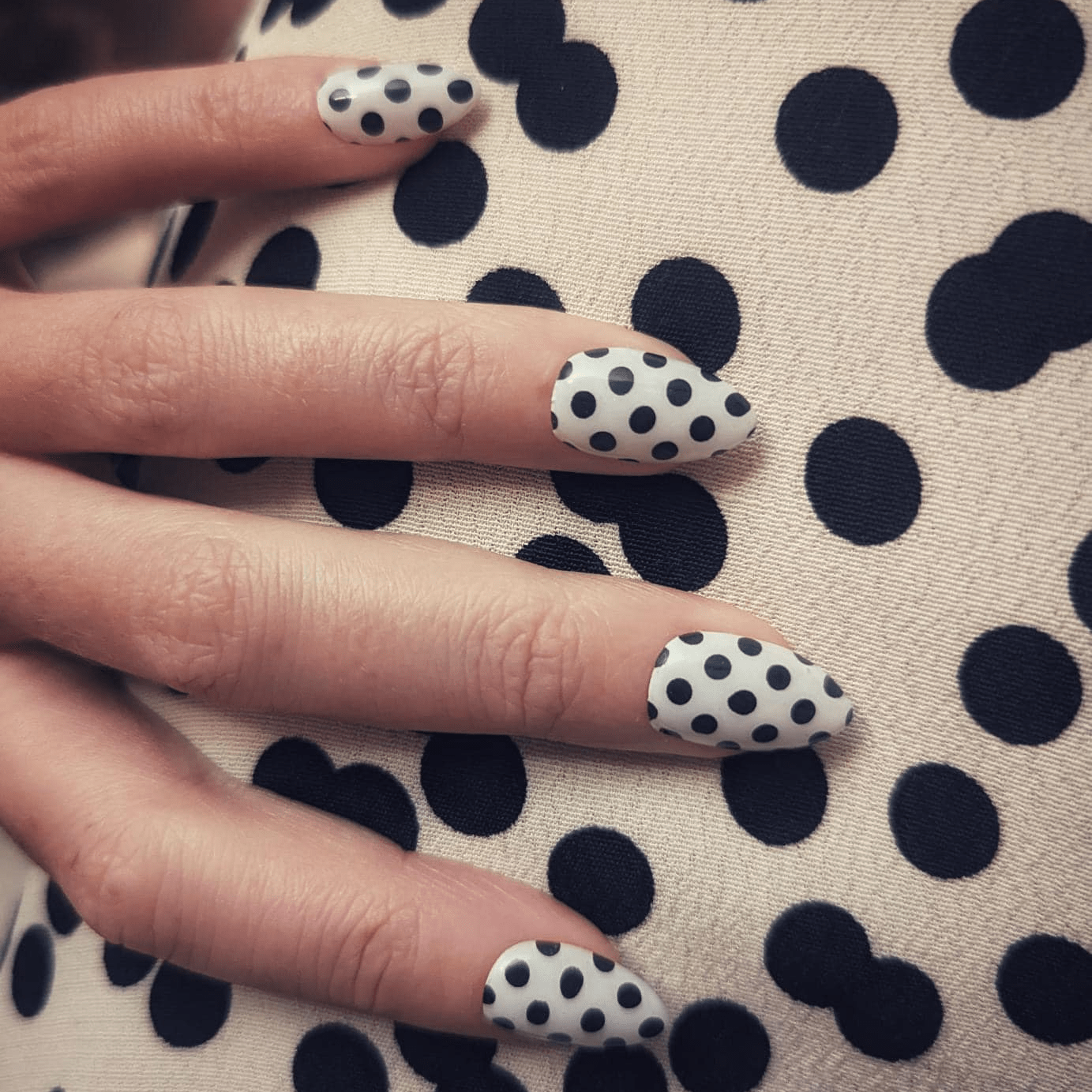 Hand wearing black and white polka dot gel nail wraps with retro spotty design