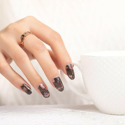 Dark floral nail wraps on hand featuring black background with pink botanical patterns