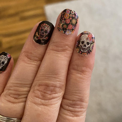 Halloween skull nail wraps with pink flowers and black background on manicured hand